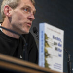 Thorsten Mense im Profil linksseitig im Bild; unten rechts unscharf das Buch "Rechts, wo die Mitte ist"